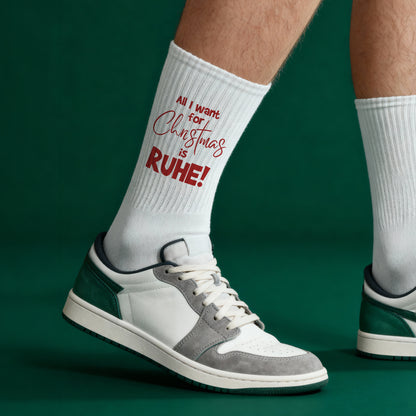 Weiße Weihnachtssocken mit rotem Spruchmotiv ‚All I want for Christmas is RUHE!‘, getragen zu sportlichen Sneakers.