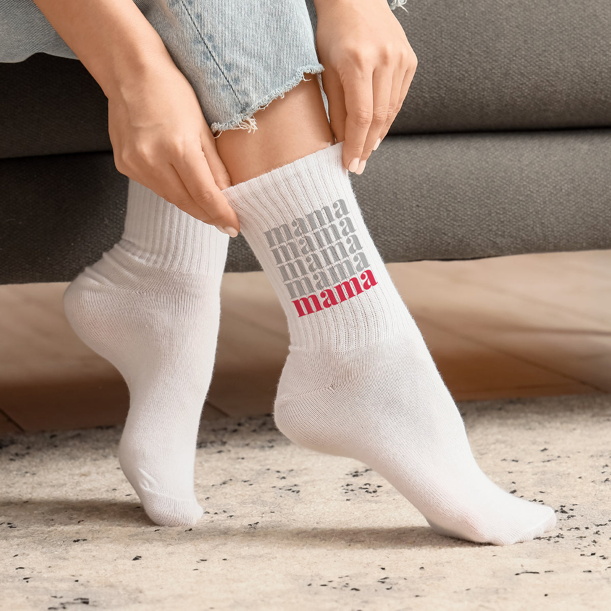 Frau zieht weiße Socken mit Mama Schriftzug in Grau und Rot an, gemütliches Setting