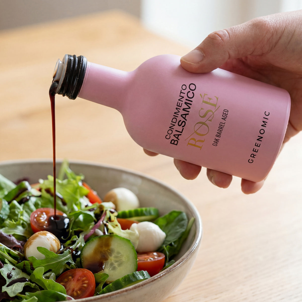 Rosafarbene Balsamico Flasche beim Eingießen über Salat