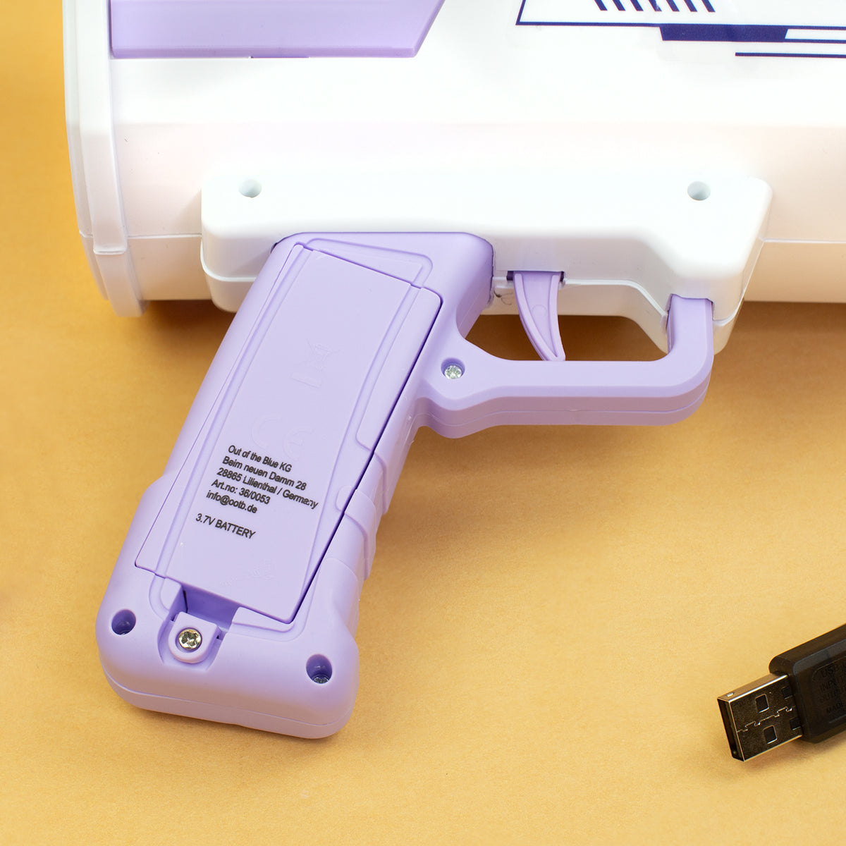 Griff der Bubble Gun mit Batteriefach und USB-Ladekabel auf gelbem Hintergrund