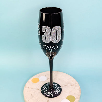 Schwarzes Sektglas mit glitzernder 30 und Ornamenten, frontal fotografiert