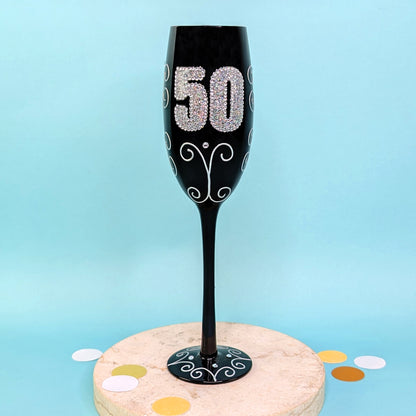 Schwarzes Sektglas mit glitzernder 50 und Ornamenten, frontal fotografiert