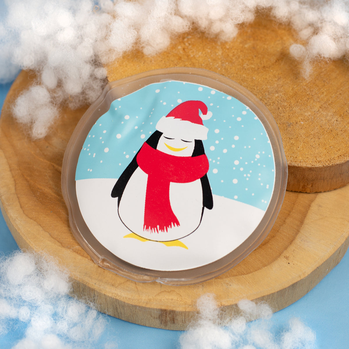 Runder Handwärmer mit Pinguinmotiv auf Holzunterlage und Kunstschnee