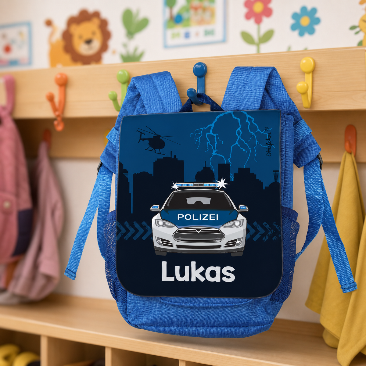 Blauer Kinderrucksack mit Polizeiauto und Name Lukas an einem Haken im Kindergarten