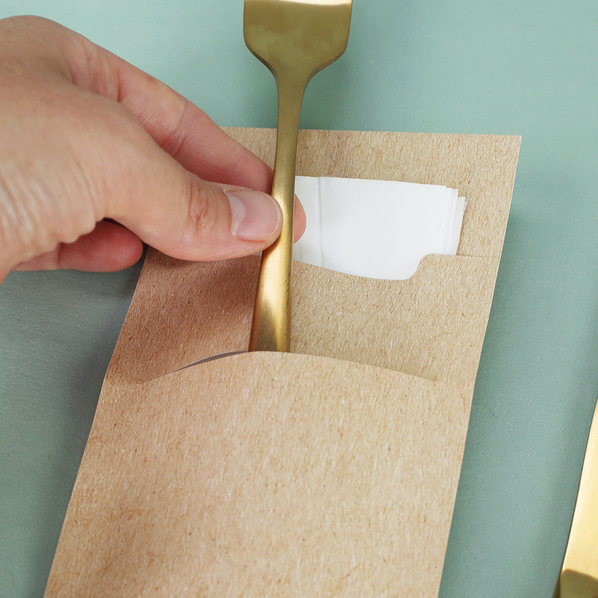 Detailaufnahme einer Bestecktasche aus Papier mit goldener Gabel und Serviette