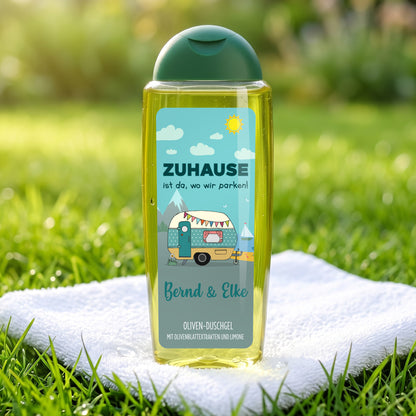 Duschgel für Camper mit Wohnwagen-Motiv und Wunschtext Melanie & Christian vor Wohnwagen und Handtuch auf Holztisch