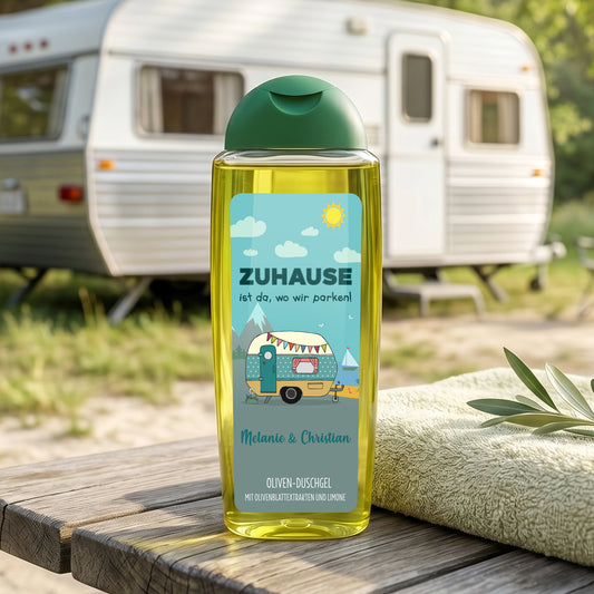 Duschgel für Camper mit Wohnwagen-Motiv und Wunschtext Melanie & Christian vor Wohnwagen und Handtuch auf Holztisch