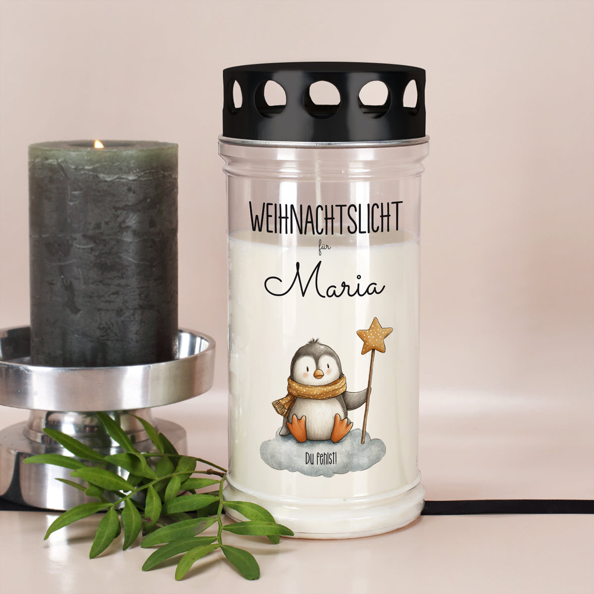 Weihnachtliches Gedenklicht mit Pinguin und Name Maria neben grauer Kerze und Grünzweig