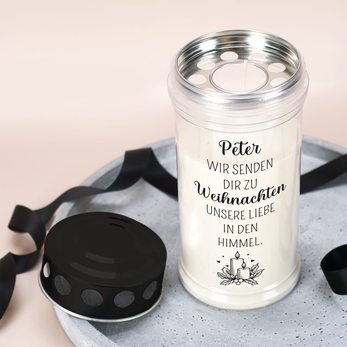 Weihnachts-Grablicht mit Spruch „Wir senden Dir zu Weihnachten unsere Liebe in den Himmel“ und Name „Peter“, offener Deckel auf Betonplatte, schwarze Schleife daneben