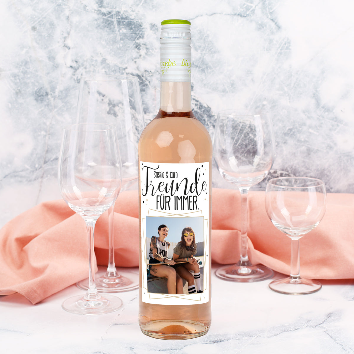 Personalisierte Roséweinflasche mit Etikett „Freunde für immer“ und Foto, dekoriert mit Gläsern und Stoff