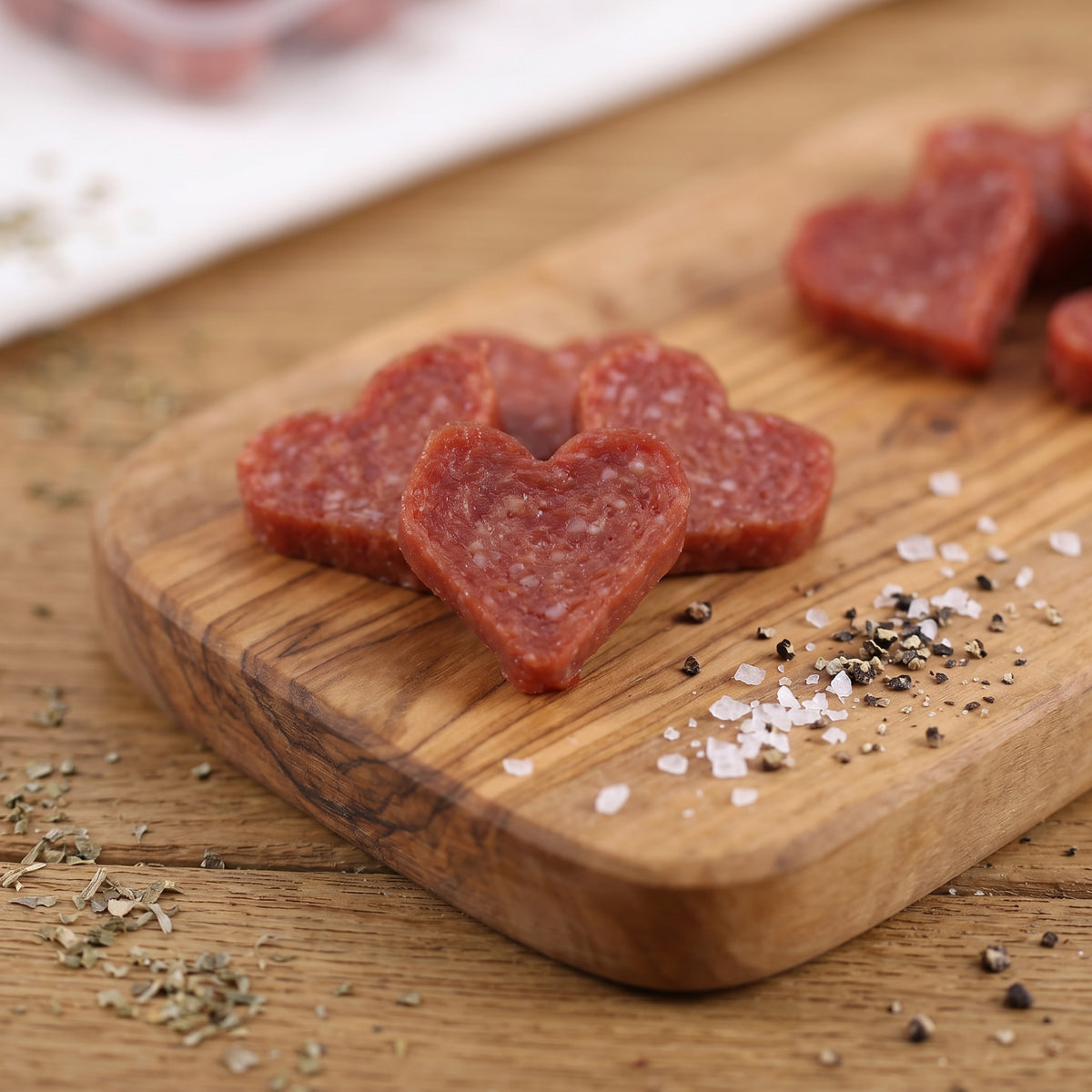 Detailaufnahme von herzförmiger Salami auf Holzbrett mit grobem Salz und Pfeffer