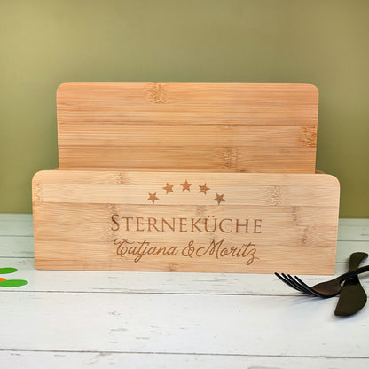 Bambusbrettchen im gravierten Halter mit „STERNEKÜCHE“-Motiv und Namen „Tatjana & Moritz“, Besteck daneben