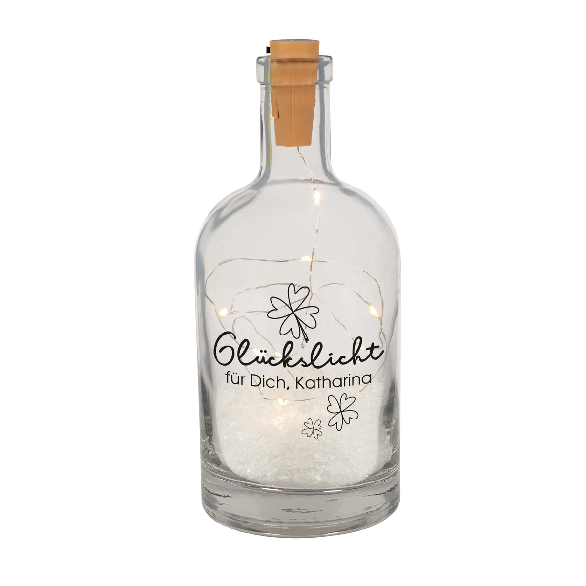 Freigestellte Glückslicht-Deko-Karaffe aus Glas mit Kleeblattmotiv, Wunschtext und integrierter LED-Lichterkette, dekoriert mit Kunstschnee.