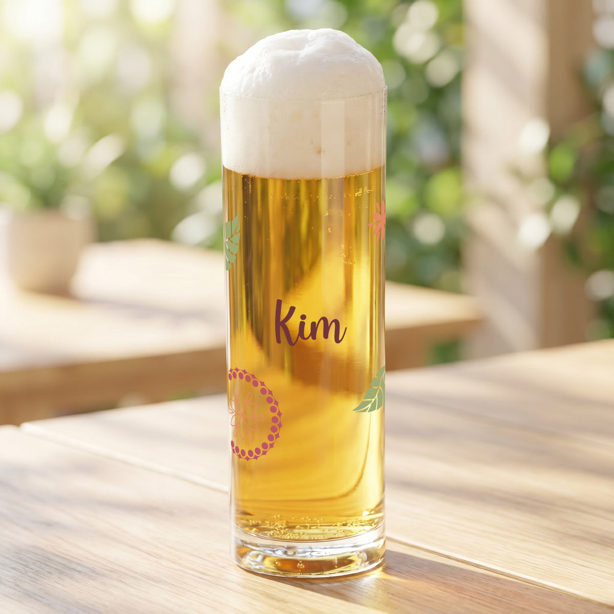 Kölschstange mit Blumen- und Blättermotiv sowie Name Kim, gefüllt mit Bier auf hellem Holztisch