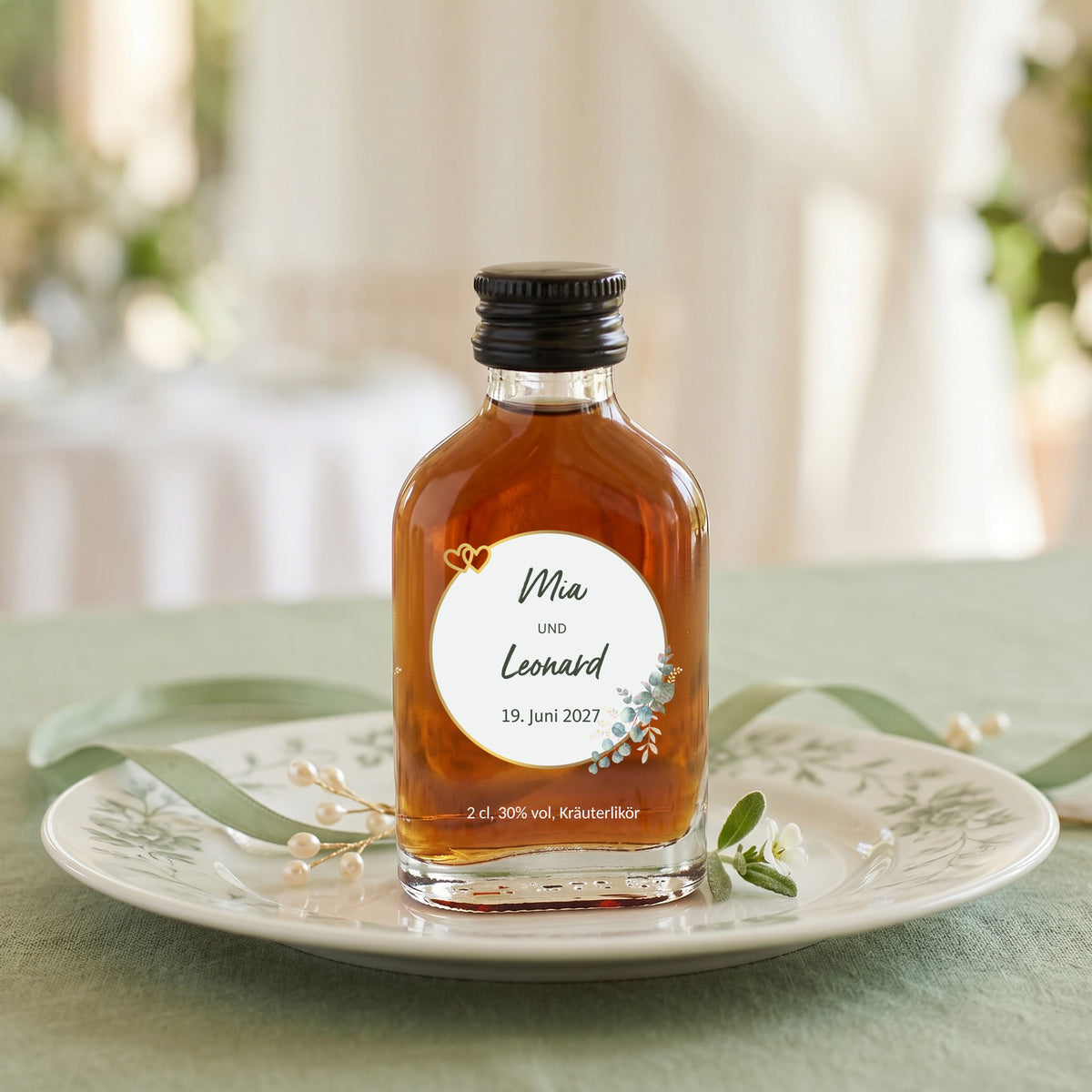 Personalisierter Kräuterlikör mit Namen Mia und Leonard und Datum 19. Juni 2027 auf grün gedecktem Hochzeitsteller
