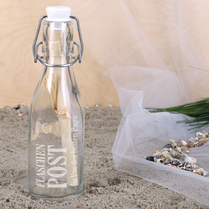 Flaschenpost Geschenkidee mit Glasflasche, Brief und maritimer Dekoration auf Sand