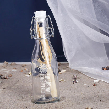 Glasflasche mit Bügelverschluss und eingerollter Geburtstagspost auf weißem Hintergrund als Geschenkidee
