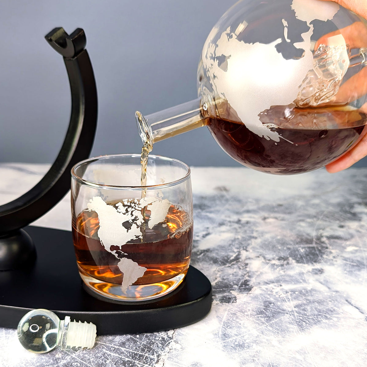 Whisky wird aus der Weltkugel-Karaffe in ein Glas mit Weltkarten-Gravur eingeschenkt – mit Aromaverschluss und Halterung