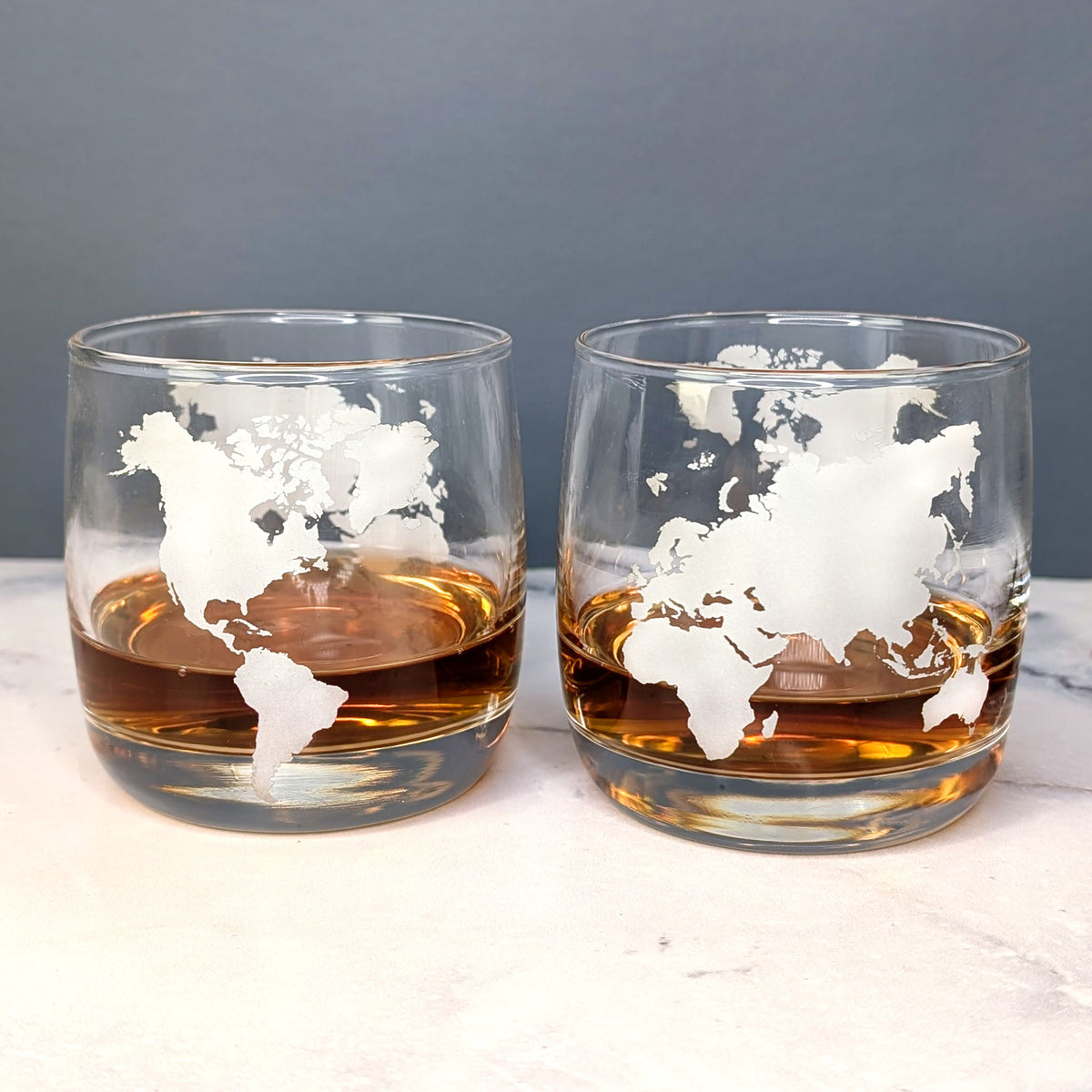 Zwei Whiskygläser mit eingeätztem Weltkarten-Design nebeneinander auf weißem Untergrund