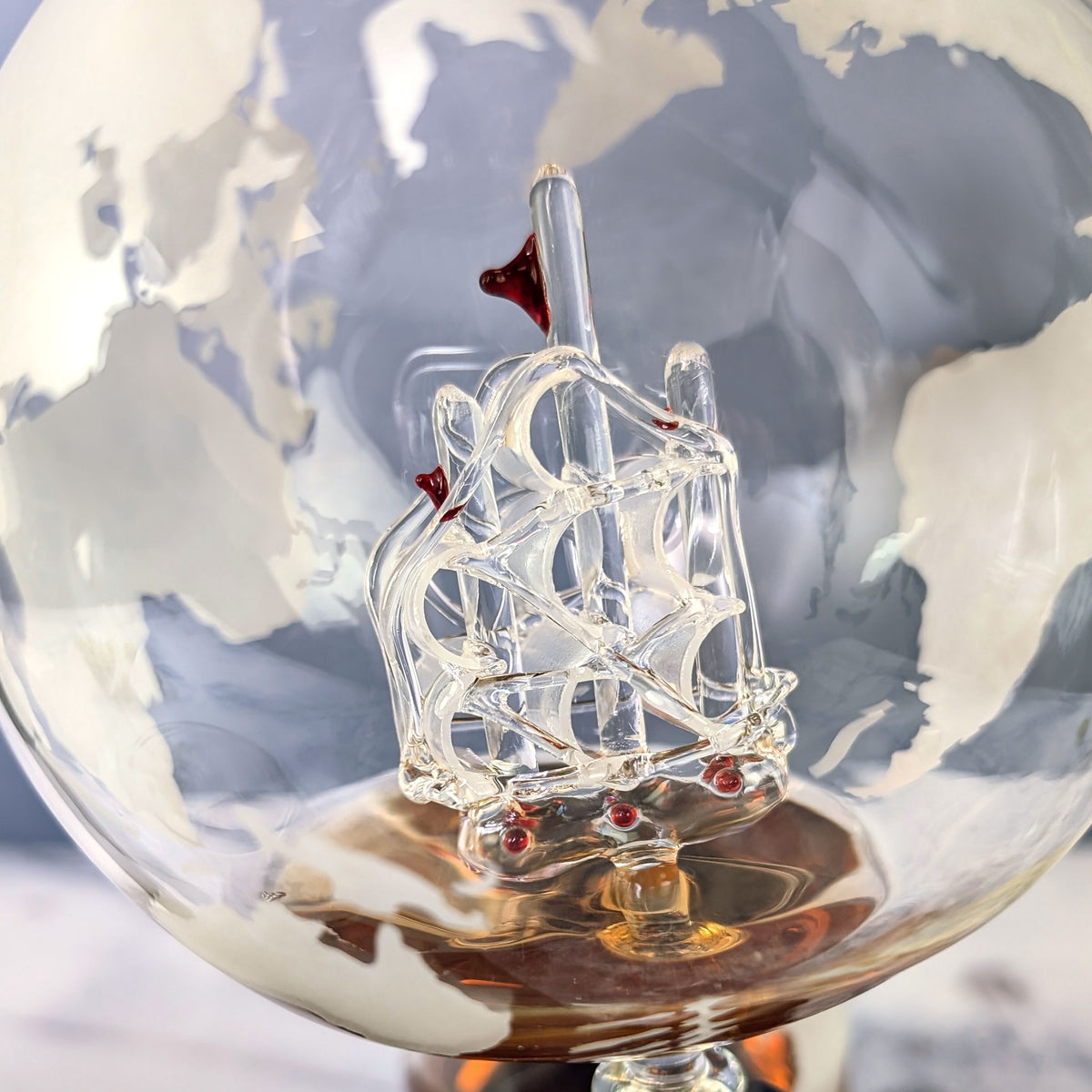 Nahaufnahme des filigranen Glas-Segelschiffs im Inneren des Weltkugel-Dekanters mit gravierter Weltkarte
