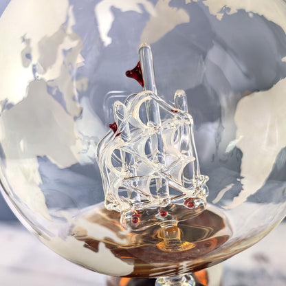 Nahaufnahme des filigranen Glas-Segelschiffs im Inneren des Weltkugel-Dekanters mit gravierter Weltkarte
