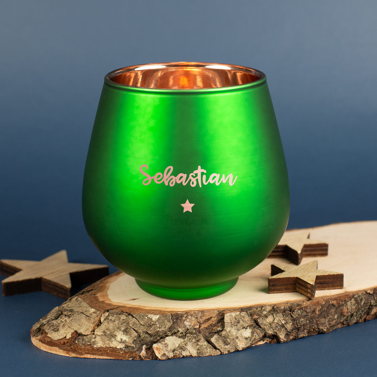 Grünes Windlicht mit Gravur „Sebastian“ und Sternmotiv, auf Holzscheibe mit Sternendeko.