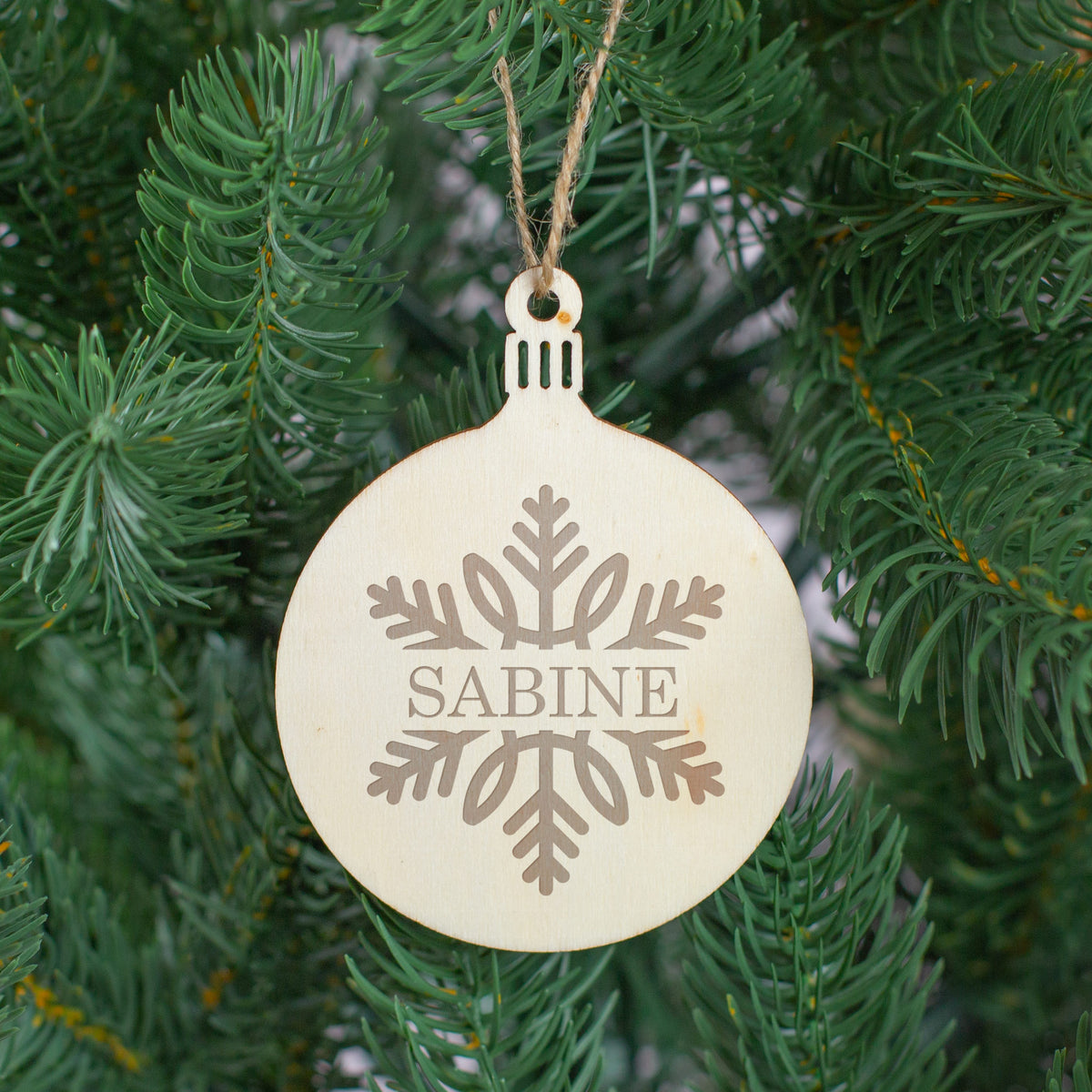 Weihnachtsbaumanhänger aus Holz, graviert und mit Juteschnur, als Christbaumschmuck dekoriert.