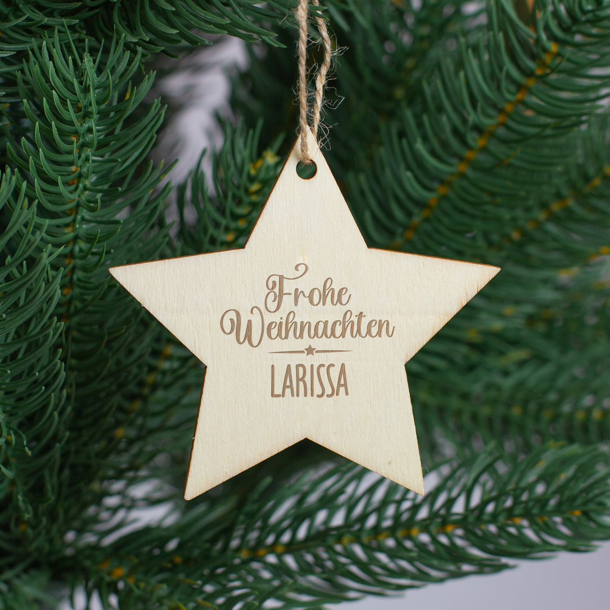 Holzstern mit Gravur „Frohe Weihnachten Larissa“ als weihnachtlicher Geschenkanhänger am Tannenbaum.