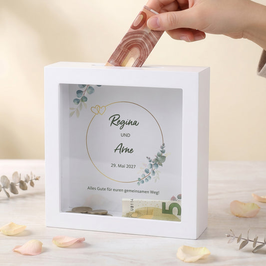 Hand steckt Geldschein in die personalisierte Hochzeits-Spardose für Regina und Arne