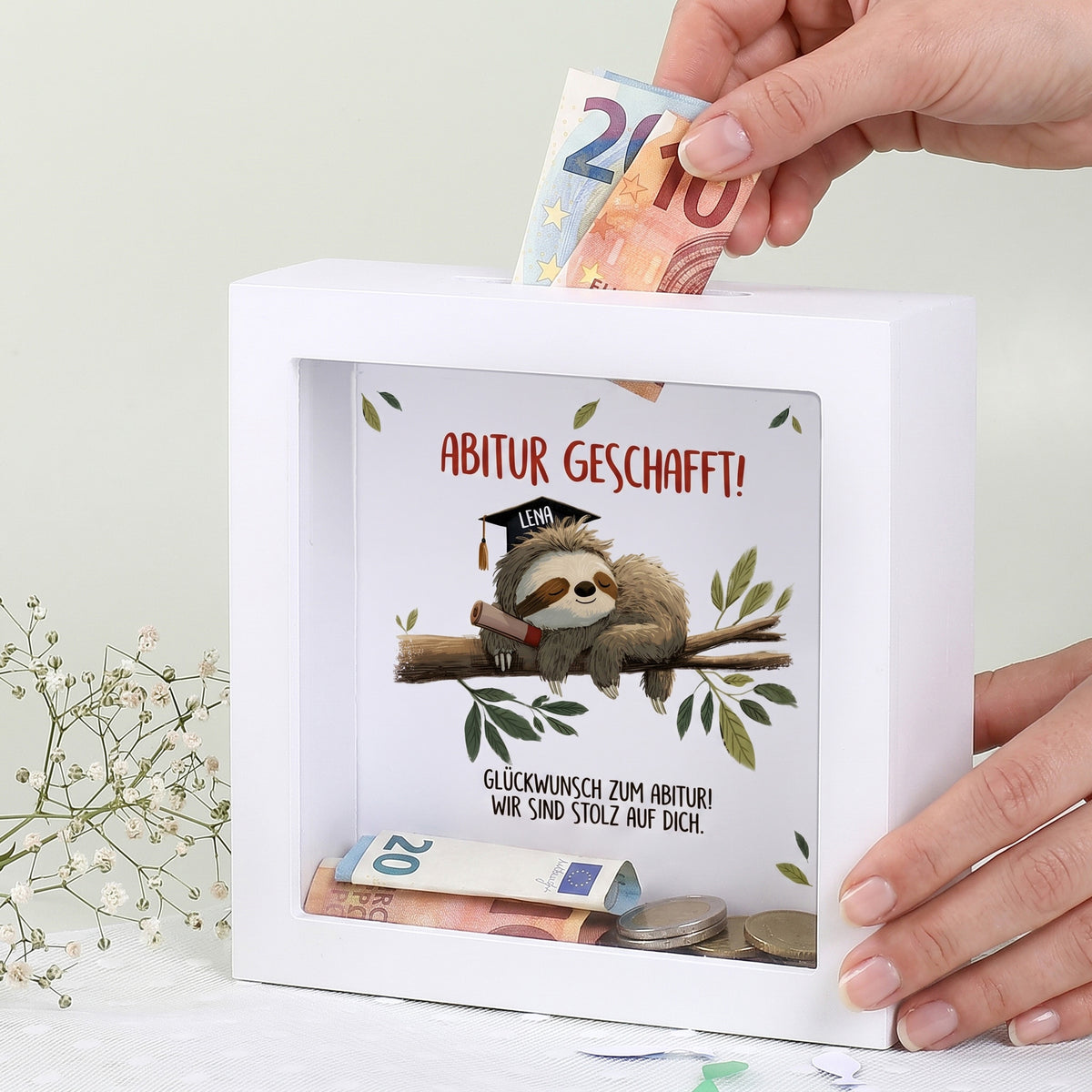 Weiße Spardose mit Faultier und Schriftzug Abitur geschafft, Name Lena und Geldschein im Einwurfschlitz