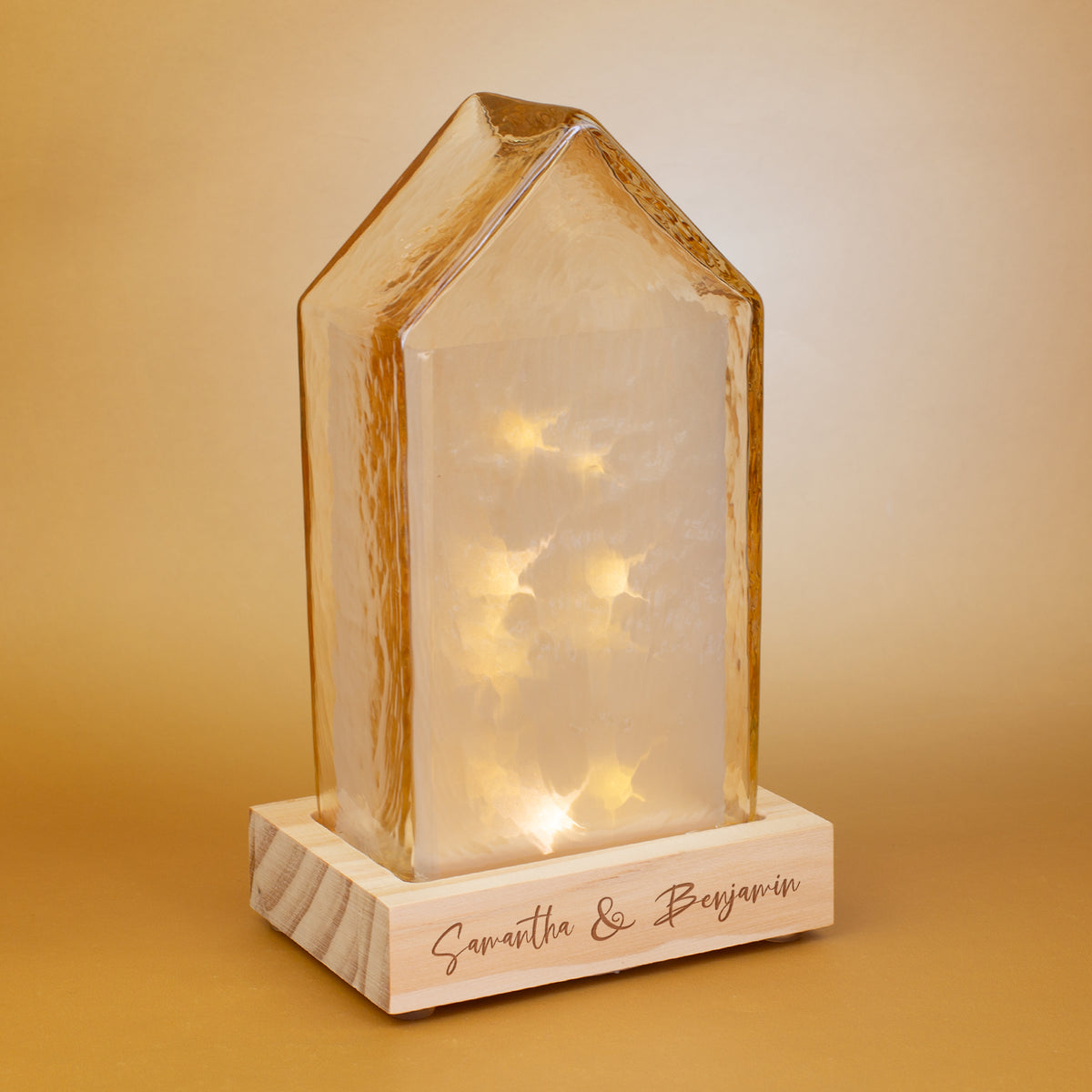 LED-Haus von Leonardo mit warmem Amberlicht und personalisierter Gravur auf dem Holzsockel – dekorative Glaslampe im modernen Hausdesign auf goldfarbenem Hintergrund.