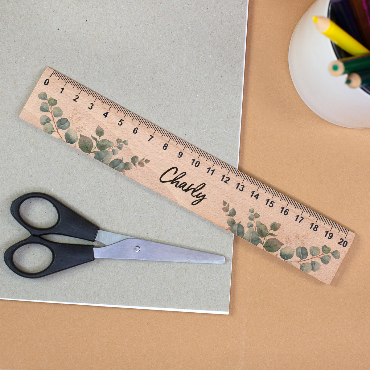 Personalisiertes Holzlineal mit Eukalyptusmotiv und Name Charly neben Schere und Stiftehalter