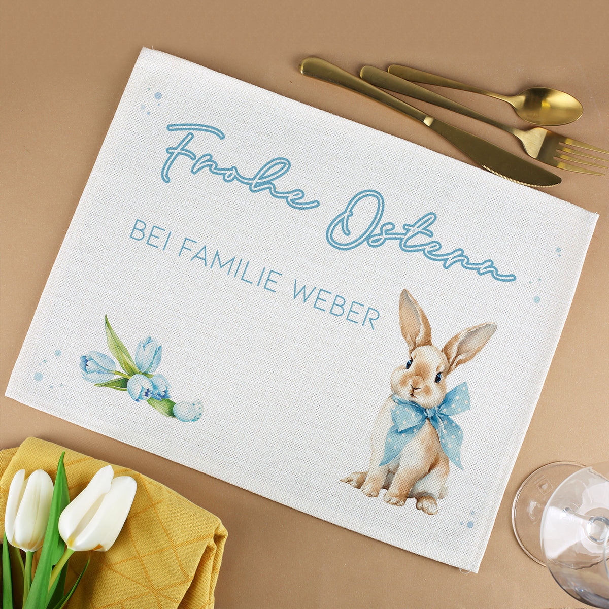 Personalisiertes Platzdeckchen aus Jute mit Hasenmotiv, Wunschtext und Frühlingsdesign neben Besteck, Tulpen und Glas