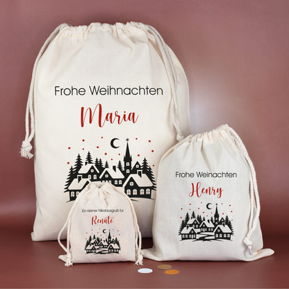 Drei Geschenksäcke in verschiedenen Größen mit Winterdorf-Motiv, roten Sternen und individuellem Wunschtext – festlich arrangiert auf bordeauxfarbenem Hintergrund.