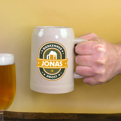 Bierkrug mit Bierkenner-Motiv wird in der Hand gehalten neben Bierglas