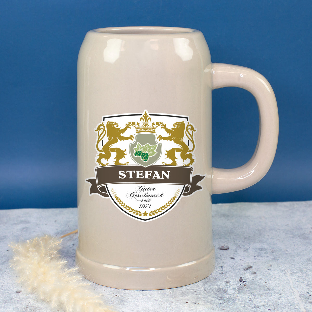 Großer Bierkrug mit Name Stefan und Wappenmotiv vor blauem Hintergrund
