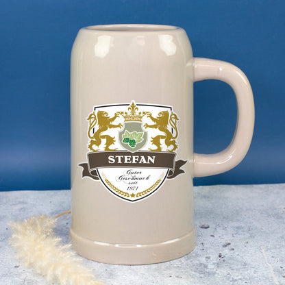 Großer Bierkrug mit Name Stefan und Wappenmotiv vor blauem Hintergrund