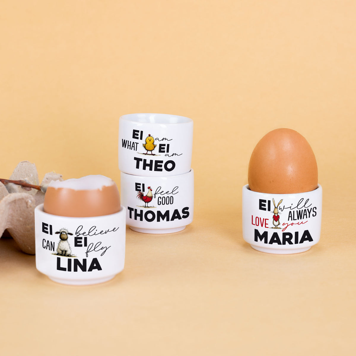 Mehrere personalisierte Eierbecher mit Namen und Oster Motiven Küken Hahn Schaf und Hase auf gelbem Hintergrund