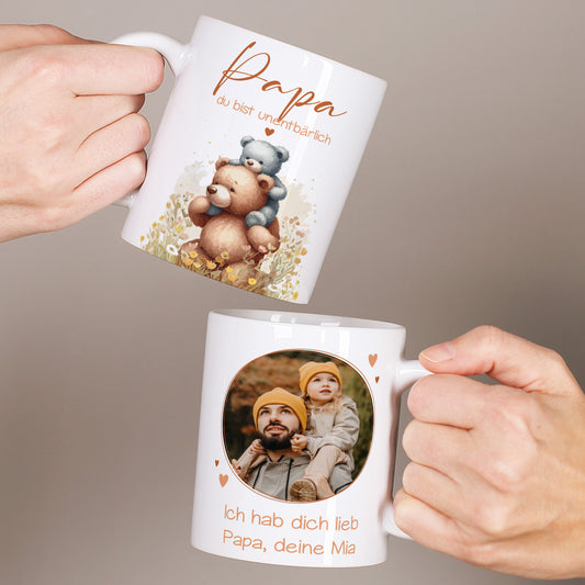 Zwei weiße Tassen werden in den Händen gehalten, links mit Bärenmotiv und dem Spruch „Papa du bist unentbärlich“, rechts mit personalisiertem Foto und Text für Papa.