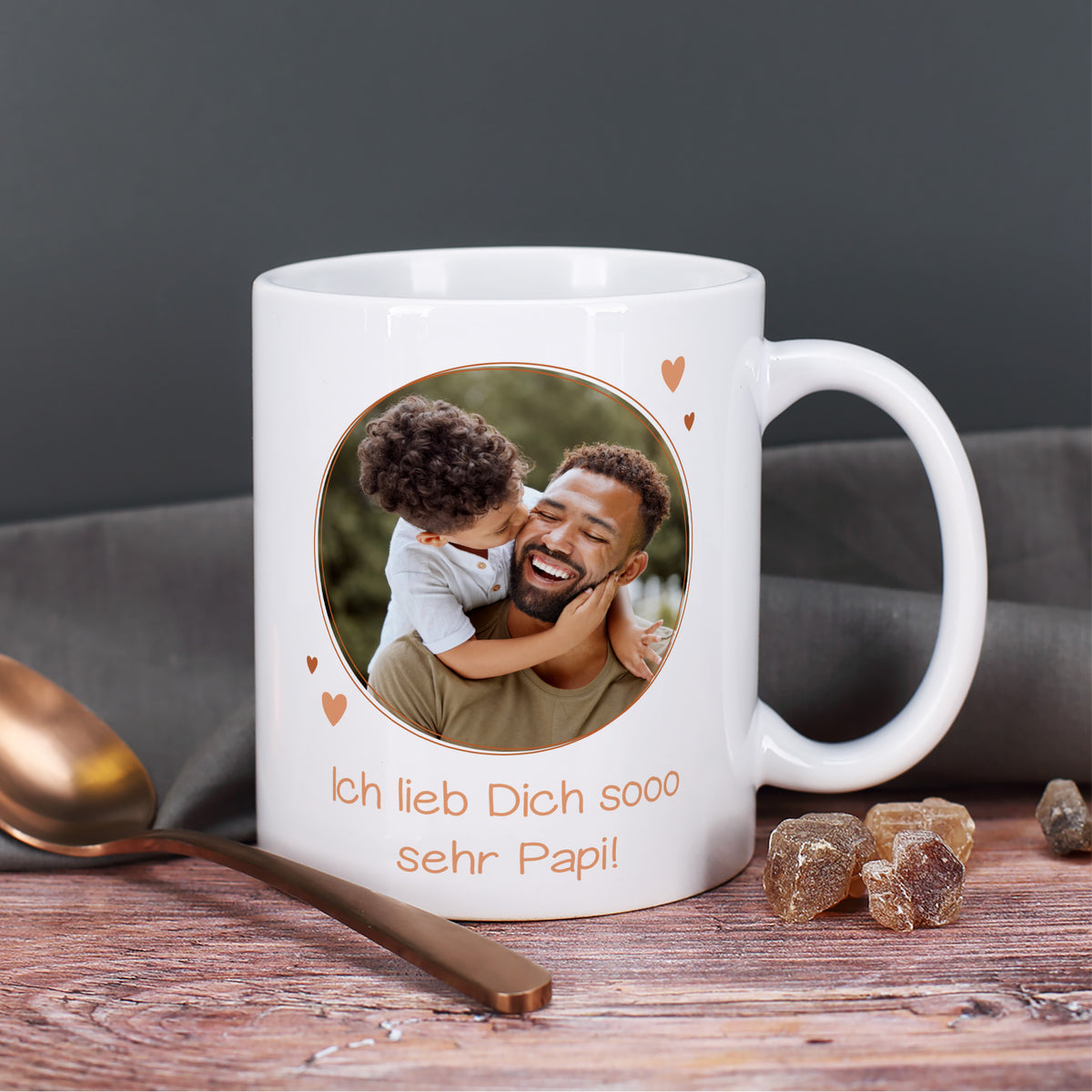 Weiße Fototasse mit rundem Foto von Papa und Kind sowie dem Text „Ich lieb Dich sooo sehr Papi!“ auf Holztisch mit Löffel und Kandiszucker.