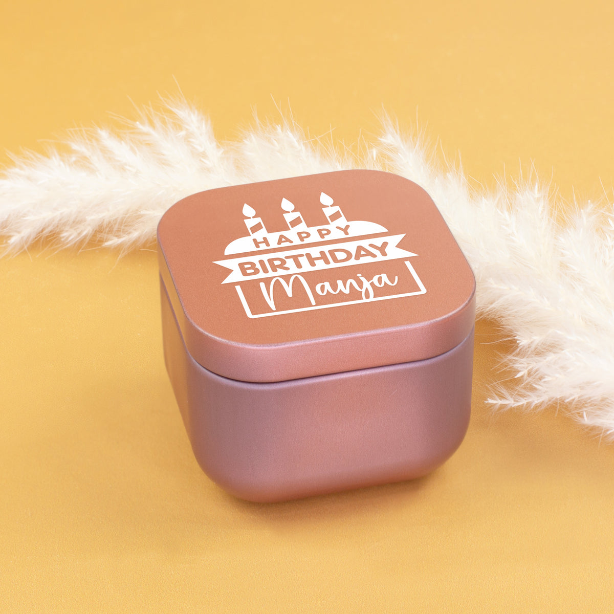 Geschlossene roségoldene Mini Duftkerze mit Happy Birthday Motiv und Name Manja auf gelbem Hintergrund