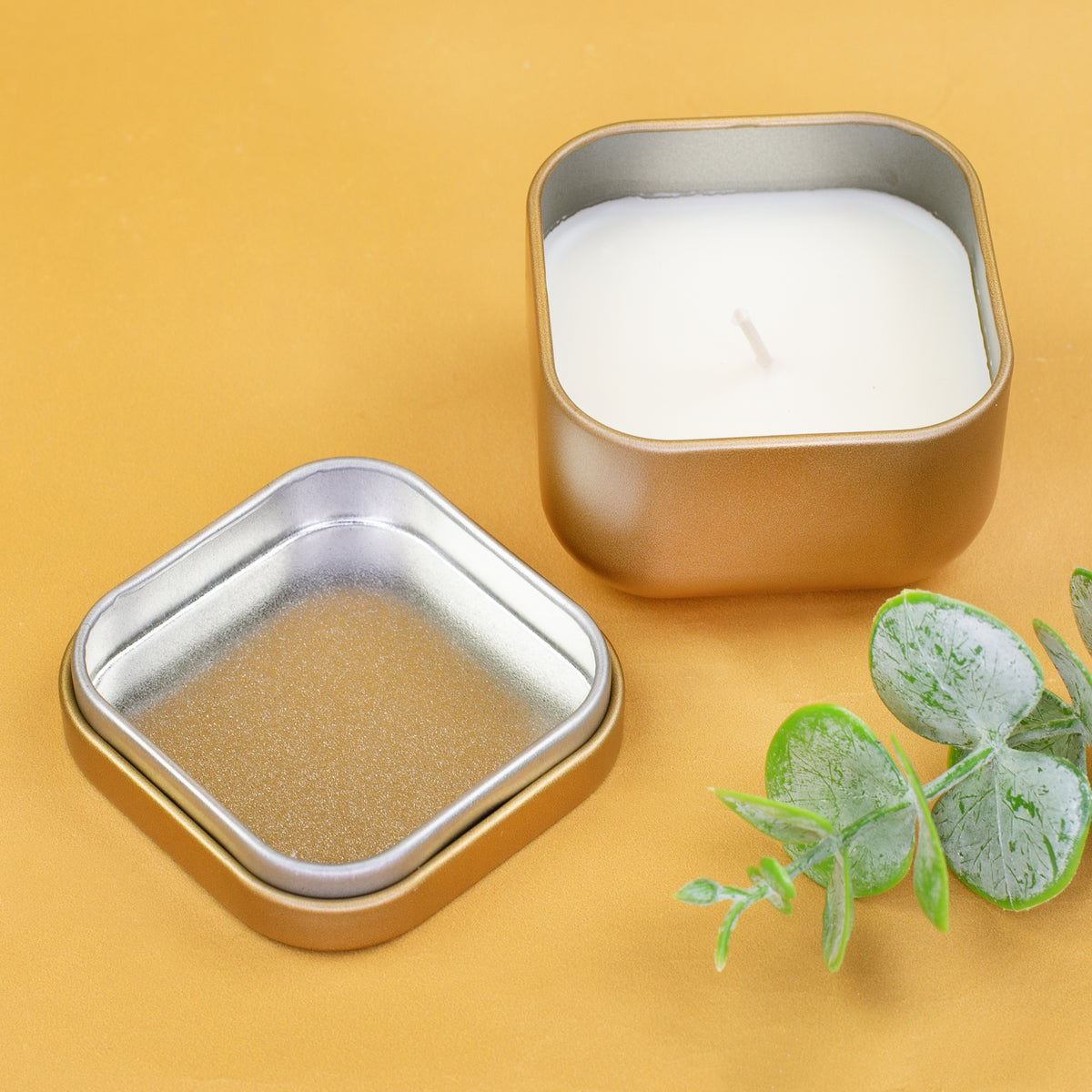 Geöffnete Mini Duftkerze in Gold mit Metalldeckel und Vanillewachs auf gelbem Hintergrund