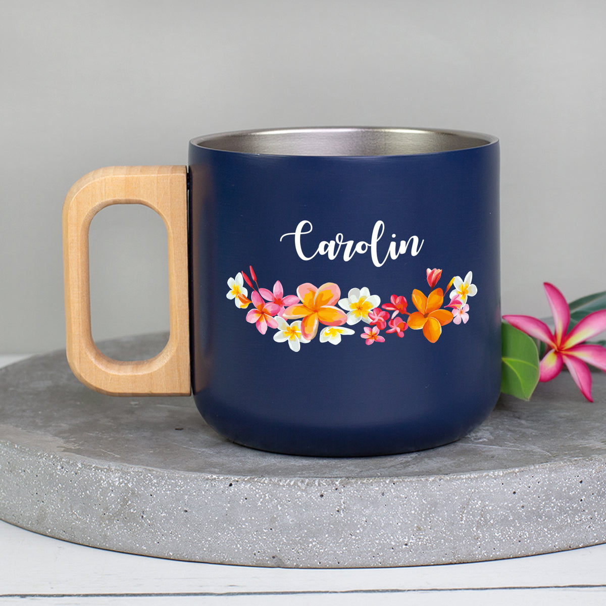 Dunkelblaue Metalltasse mit Holzgriff, tropischem Blumen-Motiv und Name Carolin auf Betonuntergrund