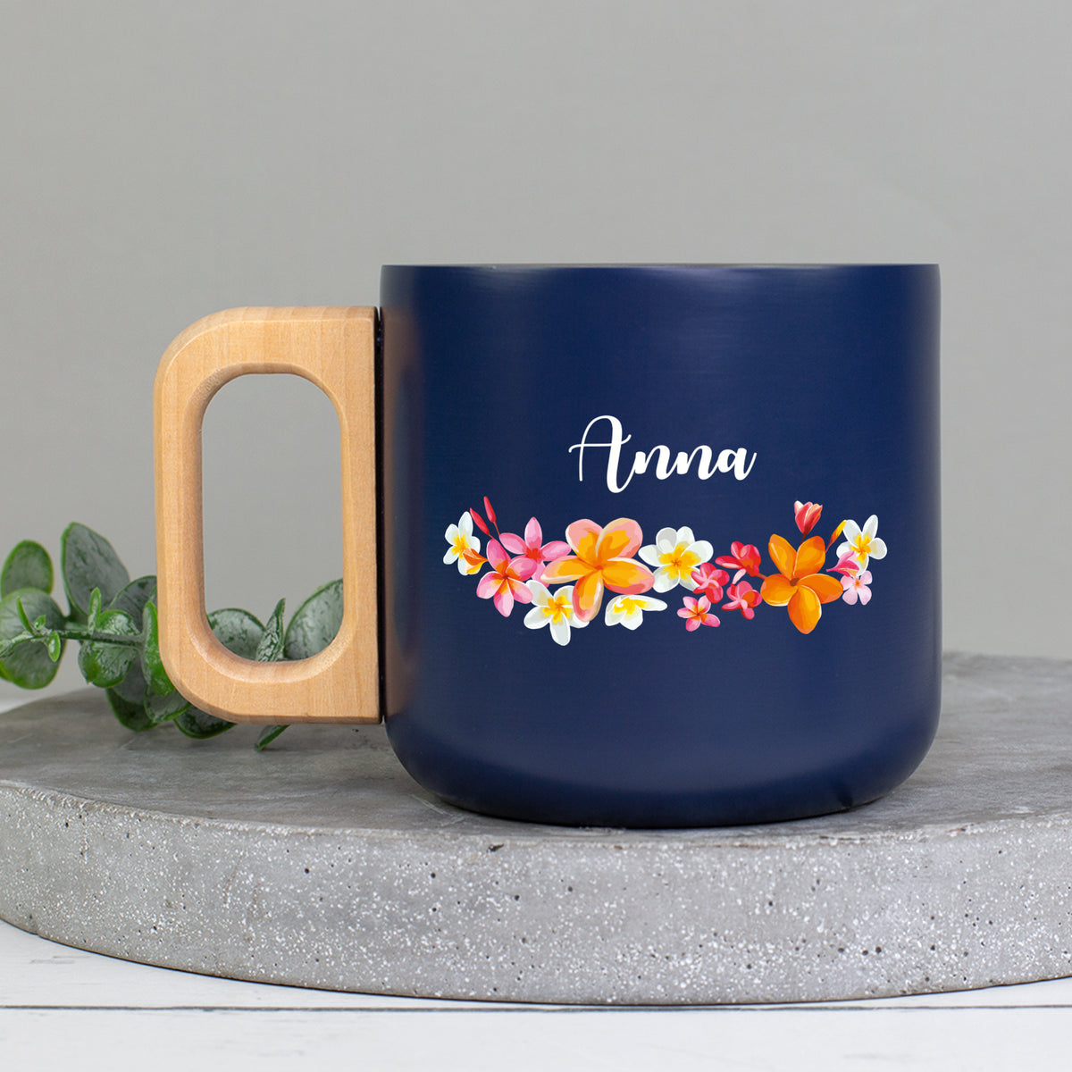 Personalisierter Edelstahlbecher mit Name Anna, bunten Blüten und natürlichem Holzgriff auf Betonplatte