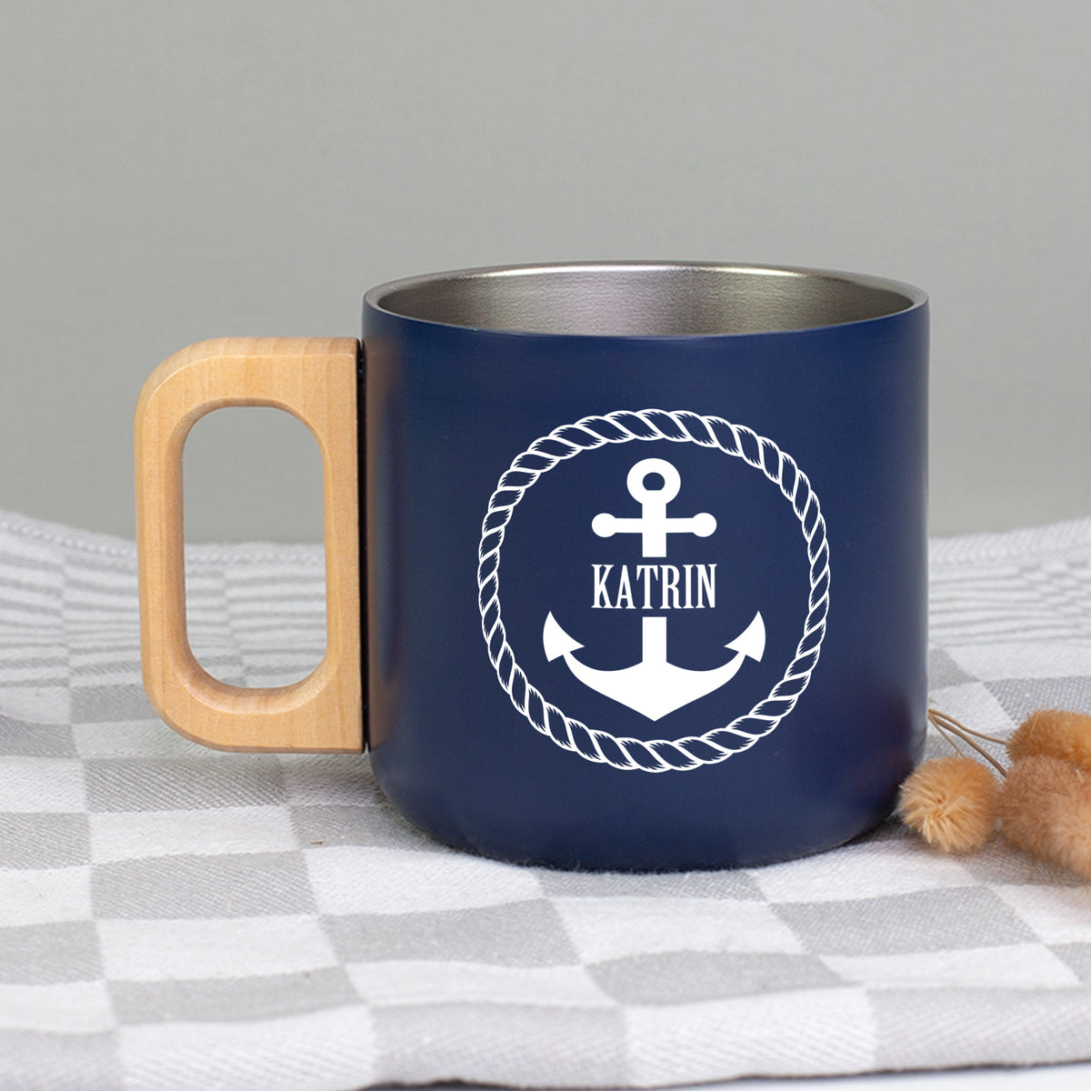 Personalisierter dunkelblauer Edelstahlbecher mit Holzgriff, Anker-Motiv und Name Katrin auf kariertem Stoff