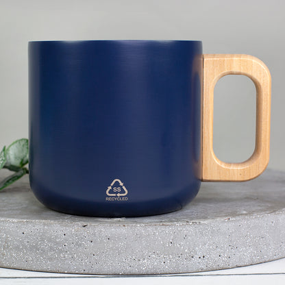 Rückseite der dunkelblauen Metalltasse mit Holzgriff und Recycled-Symbol auf Betonuntergrund