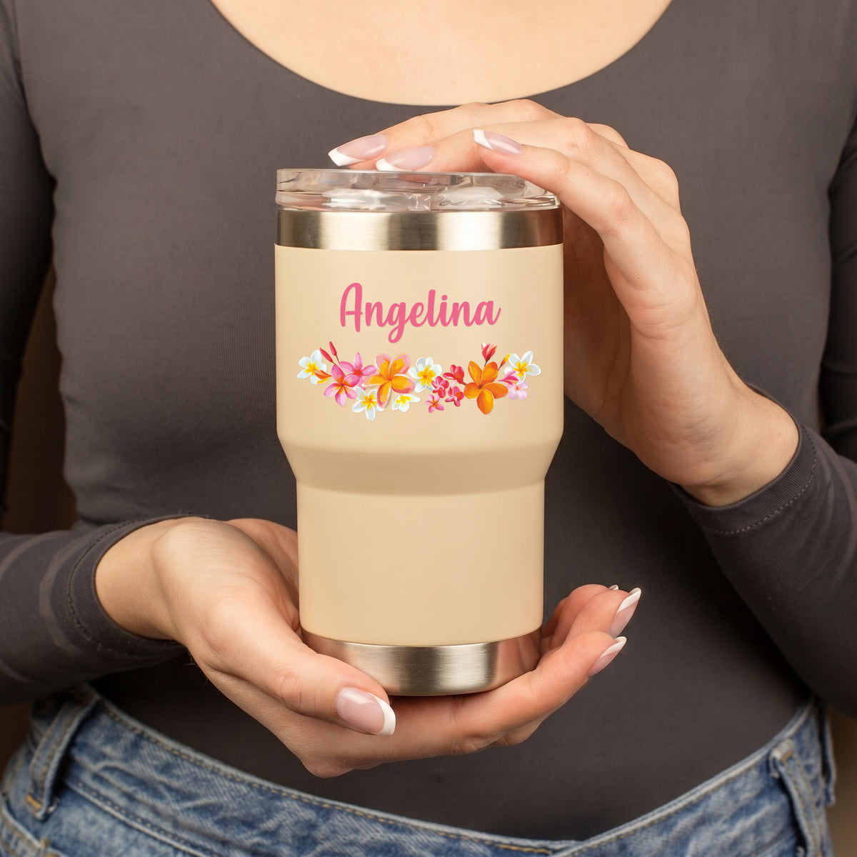 Beigefarbener Thermobecher mit Blumenmotiv und Namensaufdruck wird von einer Person in den Händen gehalten