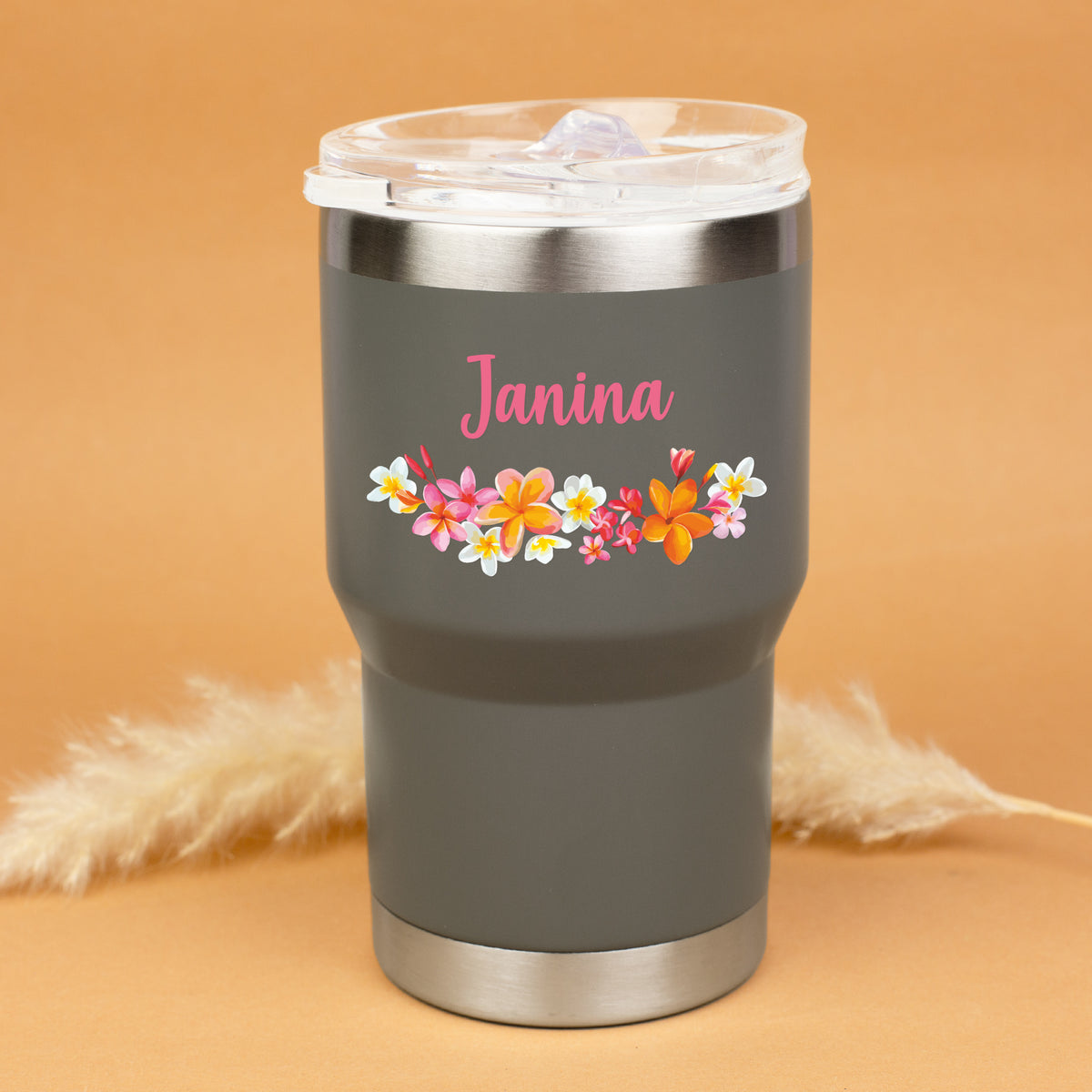 Grauer Thermobecher mit Blumenmotiv und Name Janina personalisiert vor warmem Hintergrund
