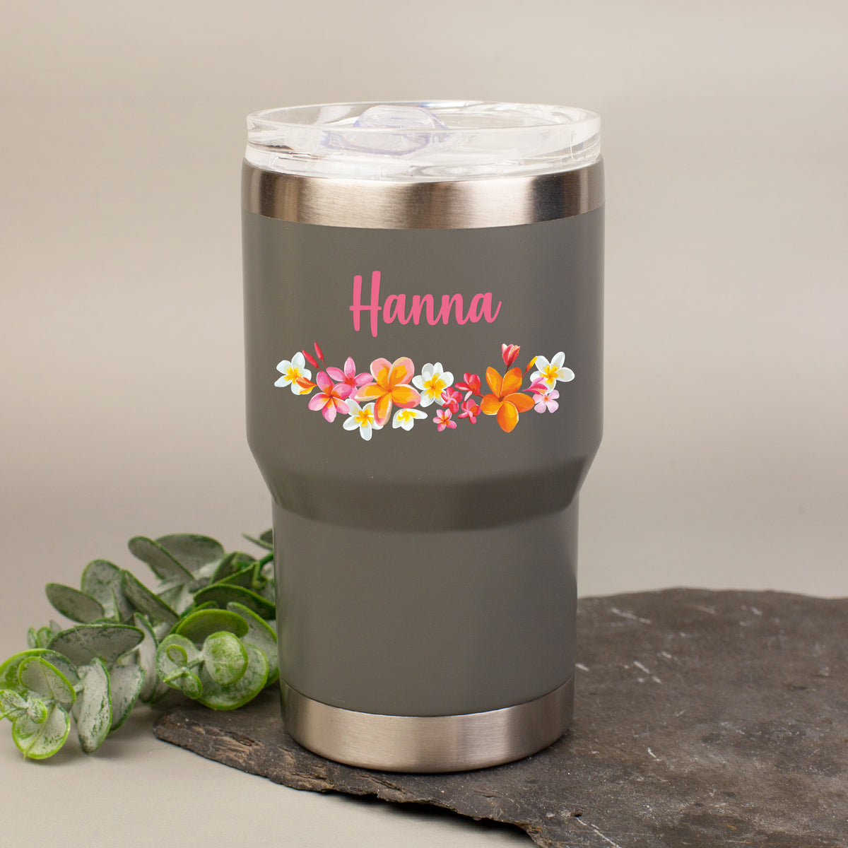 Personalisierter Thermobecher in Grau mit Blumenmotiv und Name Hanna auf dekorativer Steinplatte
