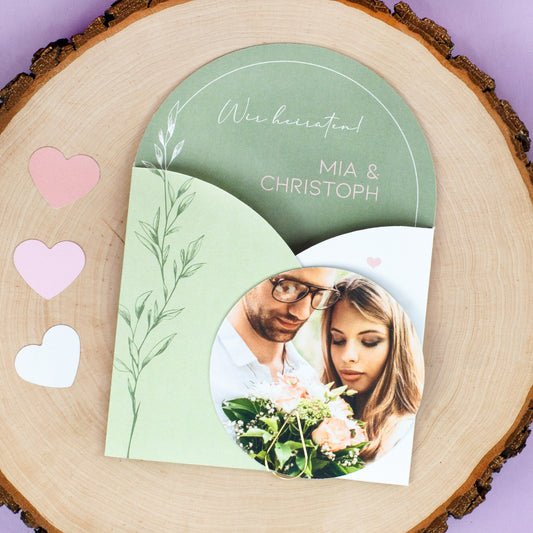 Personalisierte Hochzeitseinladung in Grün Weiß mit rundem Foto, goldener Klammer und Herzdeko auf Holzscheibe